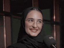a woman wearing glasses and a head scarf is smiling .