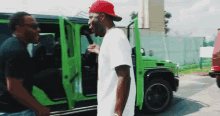 a man in a red hat is standing next to a man in a green car