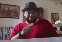 a man with a beard wearing a hat and a red shirt is giving a thumbs up .