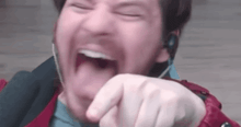 a man wearing headphones is laughing with his mouth open and pointing at the camera .