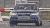 a blue audi is driving down a road in front of a royal sign