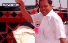a man in a white shirt is standing in front of a tent and waving his hand .