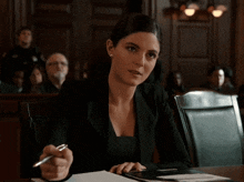 a woman in a black suit sits at a table in a court room