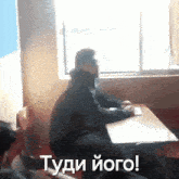 a man is sitting at a desk in front of a window with the words " tydi iogo " written on the bottom