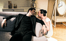 a man in a suit sits on a couch with a woman in a white dress