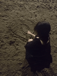 a woman drawing a heart in the sand with the letter g