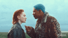 a man with blue hair talks to a woman in a leopard coat
