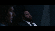 a man in a suit and tie talks to another man in a dark room and says " what the shit "