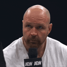 a bald man with a beard is wearing a white shirt and a microphone that says aew