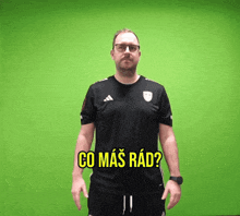 a man wearing a black adidas shirt is standing in front of a green background