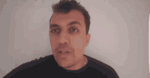 a man in a black shirt is making a funny face while standing in front of a white wall .