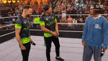 a man wearing a sweater that says find yourself talks to two other men in a wrestling ring