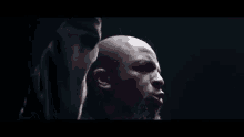 a bald man with a beard is singing into a microphone on a stage in a dark room .