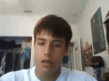 a young man in a white shirt is sitting in a room looking at the camera .