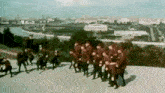 a group of soldiers are marching down a hill in front of a city skyline .
