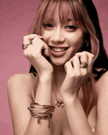 a woman with pink hair is wearing bracelets and rings on her hands .