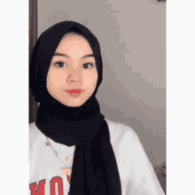 a woman wearing a black hijab and a white shirt with the letter u on it .