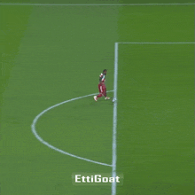 a soccer player kicks a ball on a field with the words " ettigoat " on the bottom right