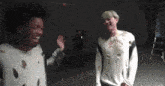 two men are standing next to each other in a dark room laughing and waving at each other .