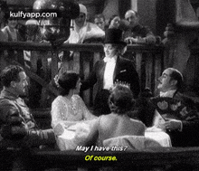 a black and white photo of a group of people sitting around a table talking to each other .