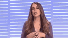 a woman with long hair is standing in front of a blue wall and talking .