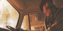 a man with a mustache is driving a truck in front of a burning building