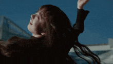 a woman 's hair is blowing in the wind and she is wearing a black jacket
