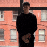 a man in a black sweater stands in front of a brick wall