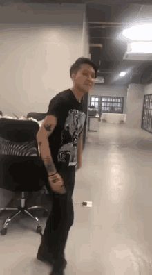a woman in a black t-shirt is dancing in a room with a chair .