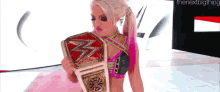 a woman in a pink top is holding a wrestling championship belt ..