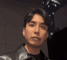 a man in a black leather jacket looks at the camera with a serious look on his face