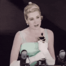 a woman in a green dress and white gloves is holding an oscar trophy .