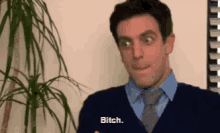 a man in a sweater and tie says bitch in front of a plant .