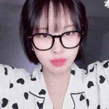 a woman wearing glasses and a polka dot shirt looks at the camera