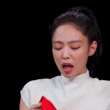 a woman in a white shirt is holding a red object in her hand and making a funny face .