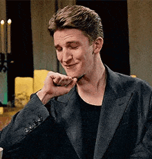 a young man in a suit is sitting at a table with his hand on his chin .
