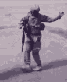 a soldier is holding a gun and waving while walking down a street .