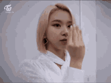 a woman with pink hair and neon green nails is making a heart with her hands .