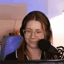 a woman wearing headphones and glasses is sitting in front of a microphone and making a funny face .