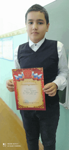 a young boy holds up a diploma with a red border