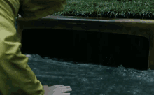 a person in a yellow raincoat reaches into a drain