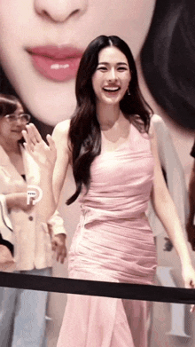 a woman in a pink dress is standing in front of a painting of a woman 's face and smiling .