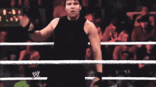 a man in a black tank top is standing in a wrestling ring with his fist in the air