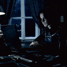 a woman is typing on a laptop in front of a window at night