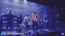a group of people singing on a stage with the word momento in the lower right corner