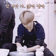 a man in an apron sits on a pottery wheel with a sign behind him that says " art of jimin "