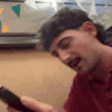 a man in a red shirt is looking at his cell phone and making a funny face .