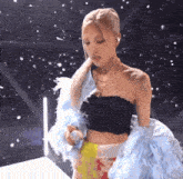 a woman wearing a black crop top and a blue feathered jacket is holding a microphone .