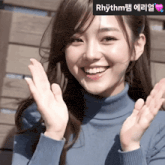 a woman in a blue turtleneck sweater is smiling with rhythm written on the bottom