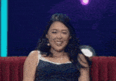 a woman in a blue tank top is sitting on a red couch smiling